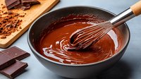 Melted dark chocolate in gray ceramic bowl with wire whisk, chocolate pieces and cocoa powder on wooden board. Homemade dessert preparation.