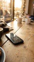 Smartphone on wooden table with warm sunlight and bokeh lights creating cozy atmosphere for morning coffee break and digital lifestyle.