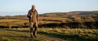 Senior man hiking with walking stick across golden countryside landscape during sunset outdoor adventure retirement lifestyle.