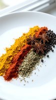 Colorful spices and herbs arranged on white plate including turmeric, paprika, star anise, black pepper and dried herbs for cooking and seasoning.