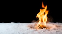 Bright orange flames dancing on white snow against dark background creating dramatic contrast between fire and ice elements for winter heating concepts.