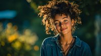 Young African American woman with curly hair smiling confidently in denim jacket during golden hour outdoor portrait session for lifestyle photography.