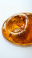 Golden amber liquid in circular glass container with swirling motion and light refraction, isolated on white background for cosmetic, skincare, or wellness product packaging design.