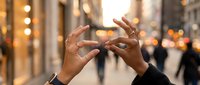 Two hands forming heart shape gesture against blurred city street with warm bokeh lights creating romantic urban evening atmosphere for love concepts.