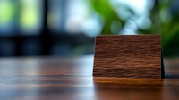 Wooden business card holder on dark wooden table with blurred green background. Elegant office desk accessory for professional workspace setting.