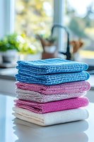 Stack of colorful kitchen towels neatly folded on countertop with sink and window in background, creating bright home atmosphere.