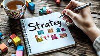 Female hand writing strategy plan with colorful diagrams in notebook, cup of tea and wooden blocks on rustic table, business planning concept for entrepreneurs.