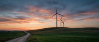 Wind turbines on green hills at sunset with dramatic orange and pink sky clouds creating renewable energy landscape for sustainable power generation.
