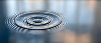Water drop creating concentric ripples on calm surface with soft bokeh background for wellness and meditation concepts.