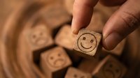 Hand holding wooden cube with smiling face among sad emoji blocks, symbolizing positivity, happiness, and mental wellness choice.