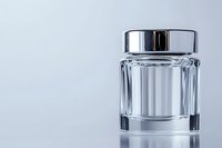 Empty glass jar with metallic silver lid on reflective surface against light background, showcasing minimalist luxury packaging design for cosmetics and skincare products.