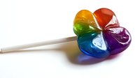 Rainbow heart-shaped lollipop candy on white stick showing vibrant spectrum of colors from red to purple, isolated against white background for confectionery designs.