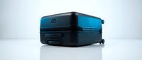 Sleek black hardshell suitcase with blue accent lighting lying on its side, showcasing modern travel luggage design on a light background.
