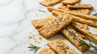 Whole grain crackers with sesame seeds and rosemary arranged on marble surface for food photography, culinary content, recipe blogs, and healthy snack marketing.
