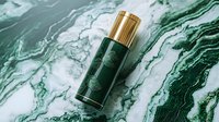 Luxurious green cosmetic bottle with gold cap on marble background. Premium skincare packaging design showcasing elegant botanical pattern on emerald surface.