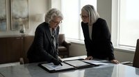 Senior women professionals reviewing documents at office table, discussing business strategy and financial reports during meeting.