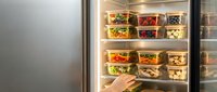 Young adult female with medium skin tone reaching for a meal prep container from an organized refrigerator shelf. Useful for nutrition, healthy eating, meal planning, and food storage content.