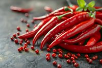 Fresh red hot chili peppers and scattered pink peppercorns on dark stone background, selective focus with natural light for food photography and culinary design.