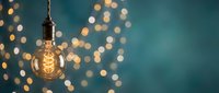 Vintage Edison bulb hanging against teal background with warm golden bokeh lights creating cozy atmospheric lighting for home decor and interior design projects.
