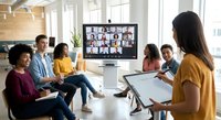 Diverse business team in modern office participating in video conference call with remote colleagues on large screen for hybrid work collaboration.