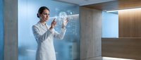 Professional female doctor in white coat interacting with futuristic holographic medical interface displaying data charts in modern hospital setting.