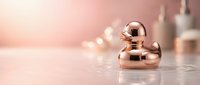 Luxurious rose gold cosmetic dropper bottle on marble surface with soft pink bokeh background for premium skincare and beauty product packaging.