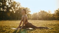 Young athletic woman practicing yoga stretching exercises outdoors in park during golden hour sunset for wellness and mindfulness meditation routine.