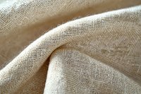 Natural linen fabric with soft folds and texture in beige color showing detailed weave pattern and gentle curves in macro photography.