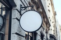 Vintage round blank signboard with ornate metal bracket mounted on stone building facade in urban setting, ready for custom branding.