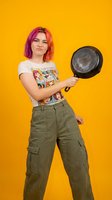Young woman with colorful pink hair holding frying pan on bright yellow background. Casual cooking concept for kitchen and culinary designs.