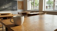 Empty classroom with coffee cup on wooden desk, blackboard and windows creating peaceful academic atmosphere for education concepts.