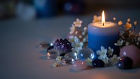 Burning blue candle surrounded by colorful gemstones and delicate flowers creates peaceful meditation and wellness atmosphere for relaxation rituals.