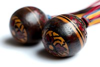 Traditional wooden maracas with tribal pattern painted in orange and red on dark brown background, close-up view showing detailed ethnic design and texture.