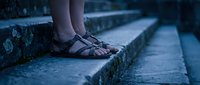 Woman feet in leather sandals standing on stone steps in evening twilight creating moody atmospheric scene for lifestyle and fashion concepts.
