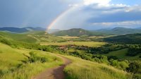 Vibrant rainbow arches over rolling green hills and winding dirt path through mountain meadow landscape. Dramatic clouds and sunlight create magical natural scenery.
