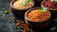 Raw organic lentils and legumes in wooden bowls garnished with fresh basil leaves on dark background, healthy protein source for vegetarian cuisine.