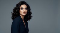 Professional businesswoman with curly hair in dark blazer against gray background for corporate marketing and leadership concepts.