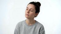 Young Caucasian woman with closed eyes in gray sweatshirt showing peaceful meditation pose against white background for wellness and mindfulness content.