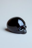 Glossy black skull sculpture with reflective surface on light background, dramatic side lighting creates mysterious atmosphere and highlights smooth contours.
