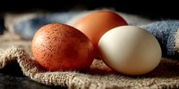 Fresh farm eggs in brown and white colors arranged on rustic burlap fabric with natural lighting for organic cooking and healthy breakfast concepts.