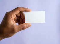 Male hand with dark skin tone holding blank white business card against lavender background, suitable for corporate branding and identity design projects.