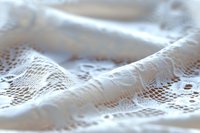 Delicate white lace fabric with intricate floral pattern creates soft folds and textures, capturing light and shadow in ethereal macro photography.