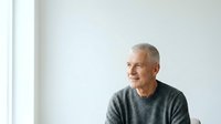 Senior man with gray hair and light skin tone wearing casual gray shirt, looking thoughtfully to the side in bright studio setting, suitable for lifestyle, wellness, and corporate communications.