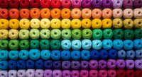 Colorful rainbow gradient thread spools arranged in organized rows creating vibrant spectrum pattern for sewing crafts textile design projects.