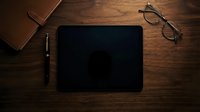 Modern workspace with black tablet, pen, glasses and leather notebook on wooden desk surface for business and productivity applications.