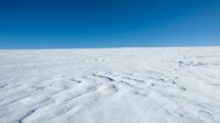 Aerial view of vast frozen landscape with snow-covered terrain and wind-carved patterns under clear blue sky, suitable for winter, climate, and nature backgrounds.