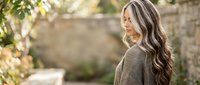 Young blonde woman with long wavy hair in cozy knit sweater enjoying peaceful moment outdoors in natural garden setting with soft sunlight filtering through.