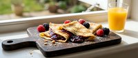 Delicious crepes filled with chocolate spread and fresh berries on wooden board with orange juice for breakfast or brunch meal.