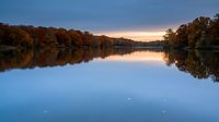 Tranquil autumn lake at sunset with colorful fall foliage reflected in calm water creating perfect mirror symmetry for nature and landscape photography.
