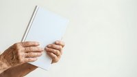 Senior adult hands holding open blank book or magazine against neutral background for publishing and reading concepts.